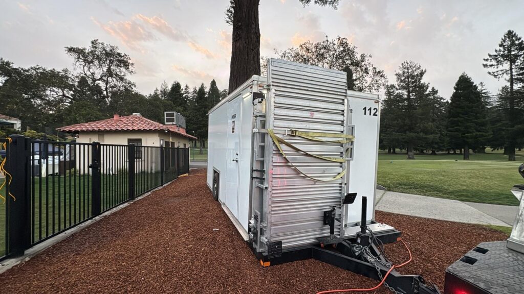 Laundry trailer hooked up to power and water on a mulch bed beside a golf course fence, The Lavatory Los Angeles