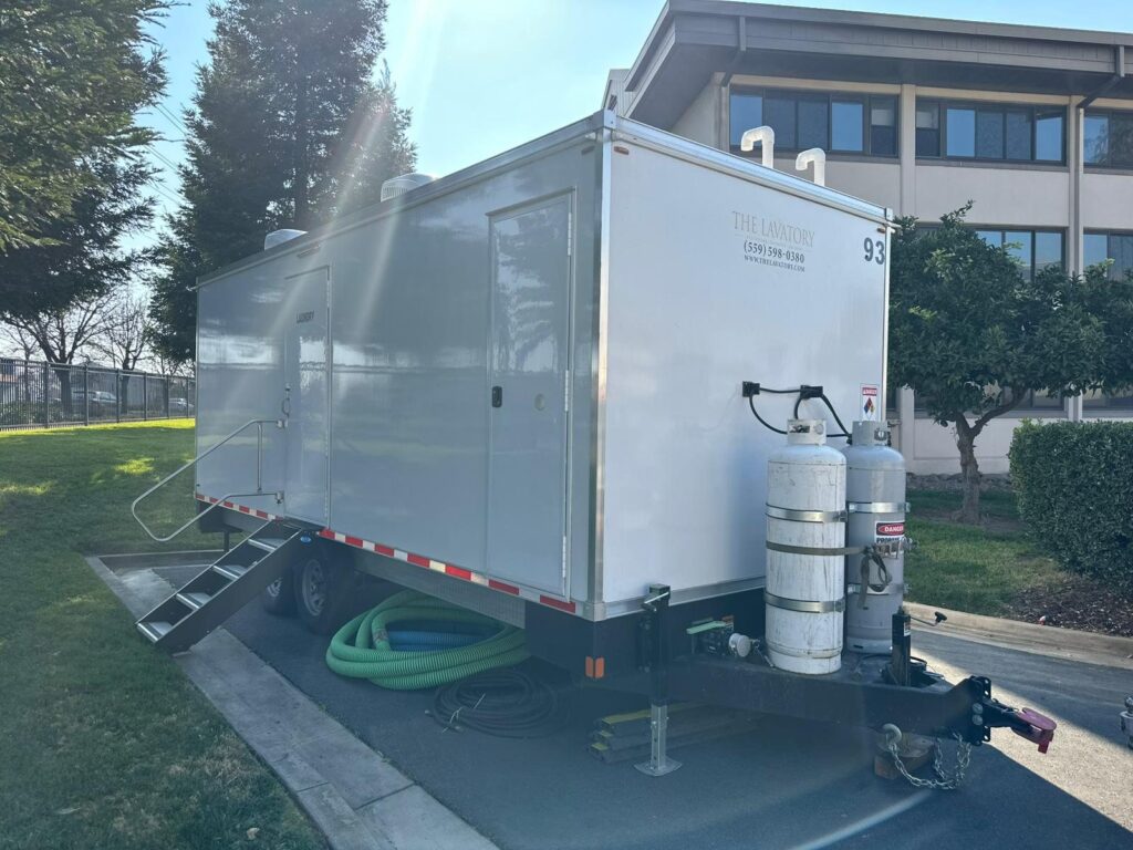 Mobile laundry trailer set on a lawn with water and drain hoses, power cords and propane tanks hooked up, The Lavatory Los Angeles