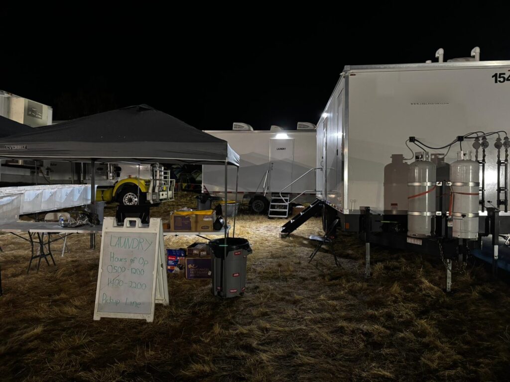 Laundry trailer lit up at night at a camp with a laundry hours sign and canopy, The Lavatory Los Angeles