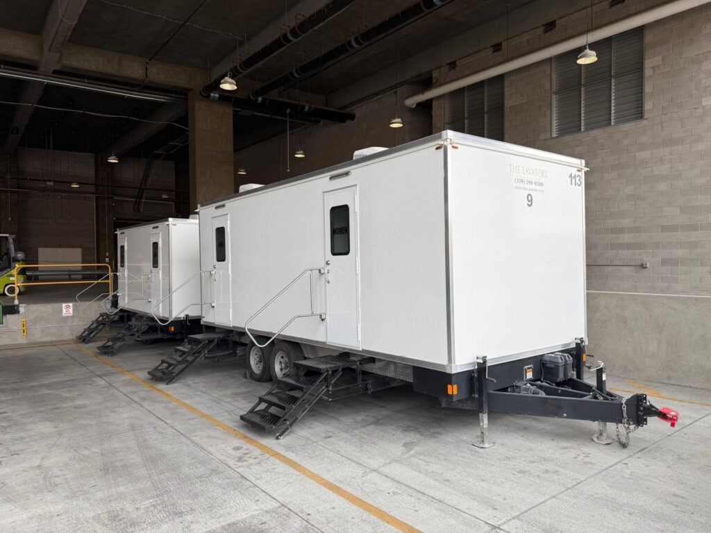 Two 9-station bathroom trailers with fold-down steps parked inside a covered loading bay, The Lavatory Los Angeles