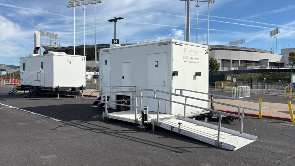 ADA plus 2 bathroom trailer with a railed ramp beside a 9-station bathroom trailer in a stadium parking lot, The Lavatory Los Angeles