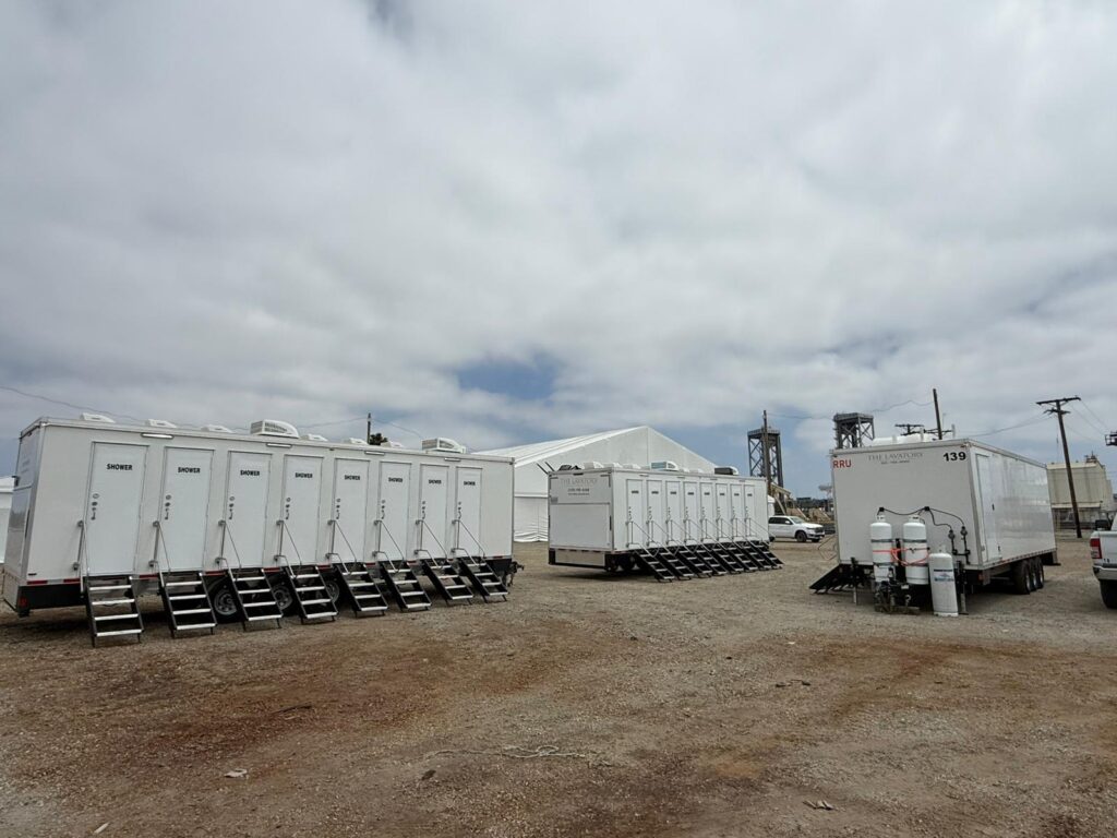 Three 8-station shower trailers with steps and propane tanks staged beside a white tent on an industrial job site in Long Beach, The Lavatory Los Angeles