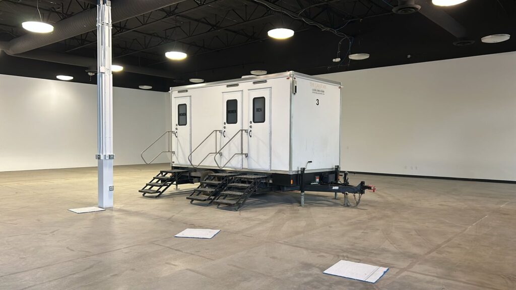 3-station bathroom trailer set up indoors on the floor of an empty event hall, The Lavatory Los Angeles