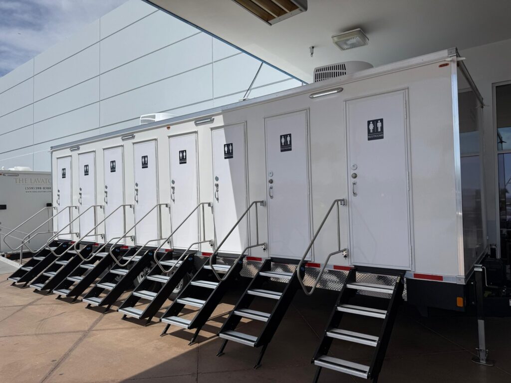 8-station private bathroom trailer with eight doors and fold-down steps parked under a building canopy, The Lavatory Los Angeles