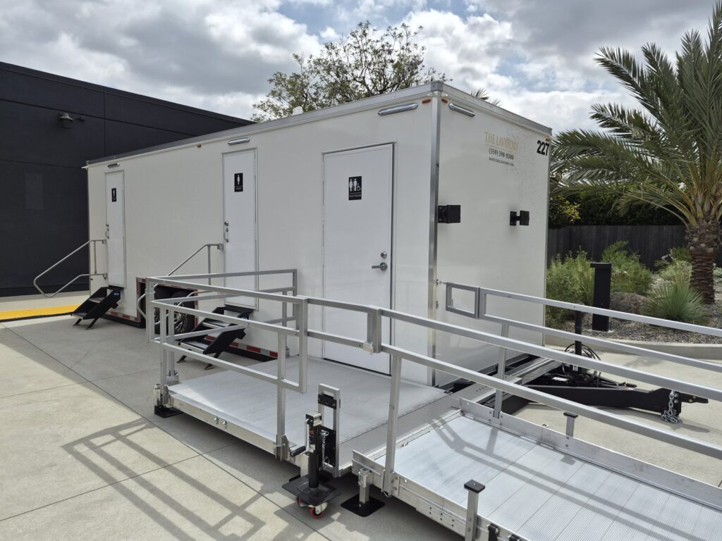 ADA plus 2 bathroom trailer with a railed wheelchair ramp and platform beside a palm tree, The Lavatory Los Angeles