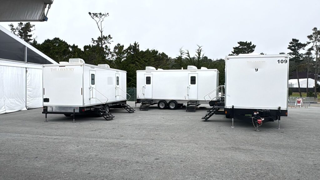 Three luxury bathroom trailers from our fleet staged together on a paved lot beside an event tent, The Lavatory Los Angeles