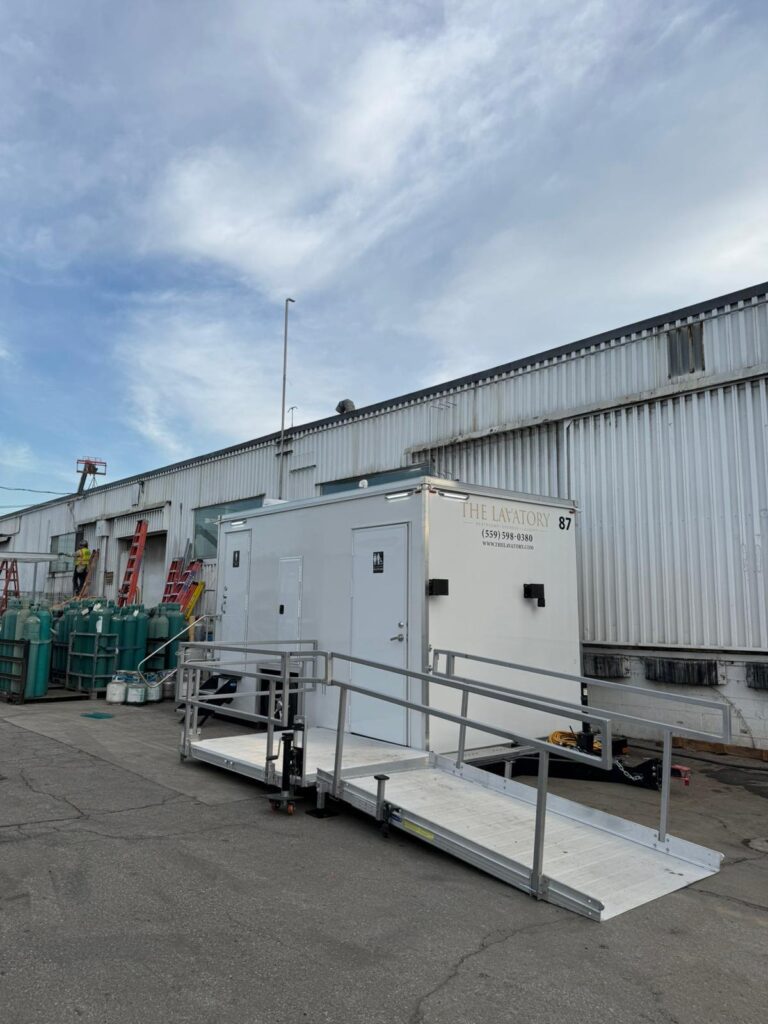 Worker on a ladder beside a warehouse where an ADA plus 2 bathroom trailer sits on a long-term rental, The Lavatory Los Angeles
