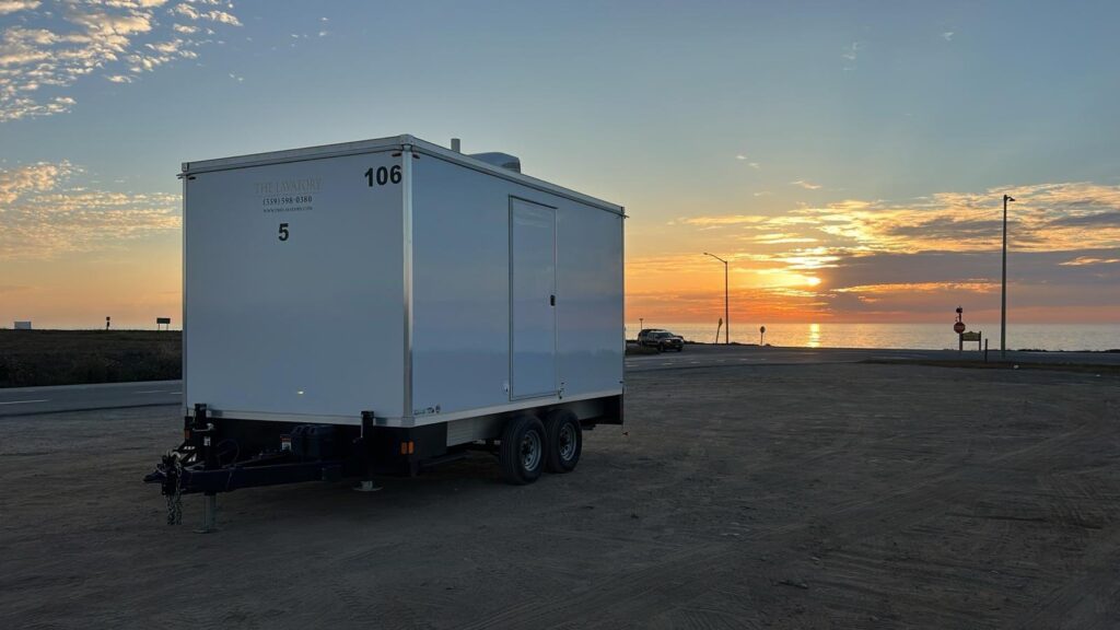 5-station bathroom trailer parked on a coastal lot at sunset with the ocean behind it, The Lavatory Los Angeles