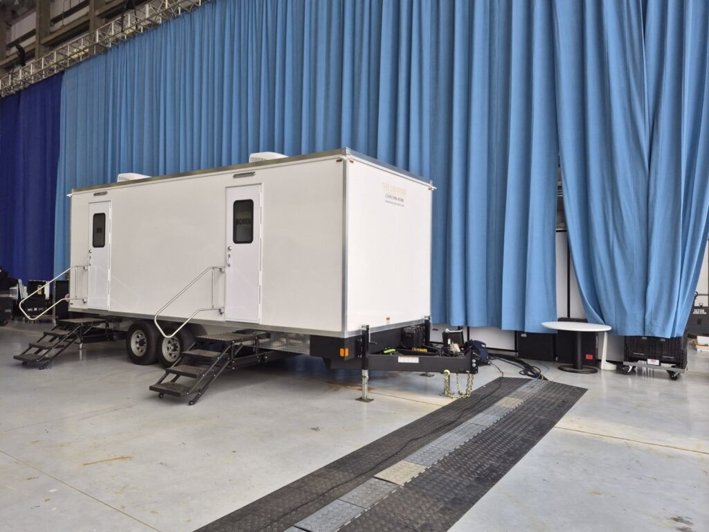 Deluxe bathroom trailer parked inside a large stage space in front of blue curtains with cable ramps on the floor, The Lavatory Los Angeles