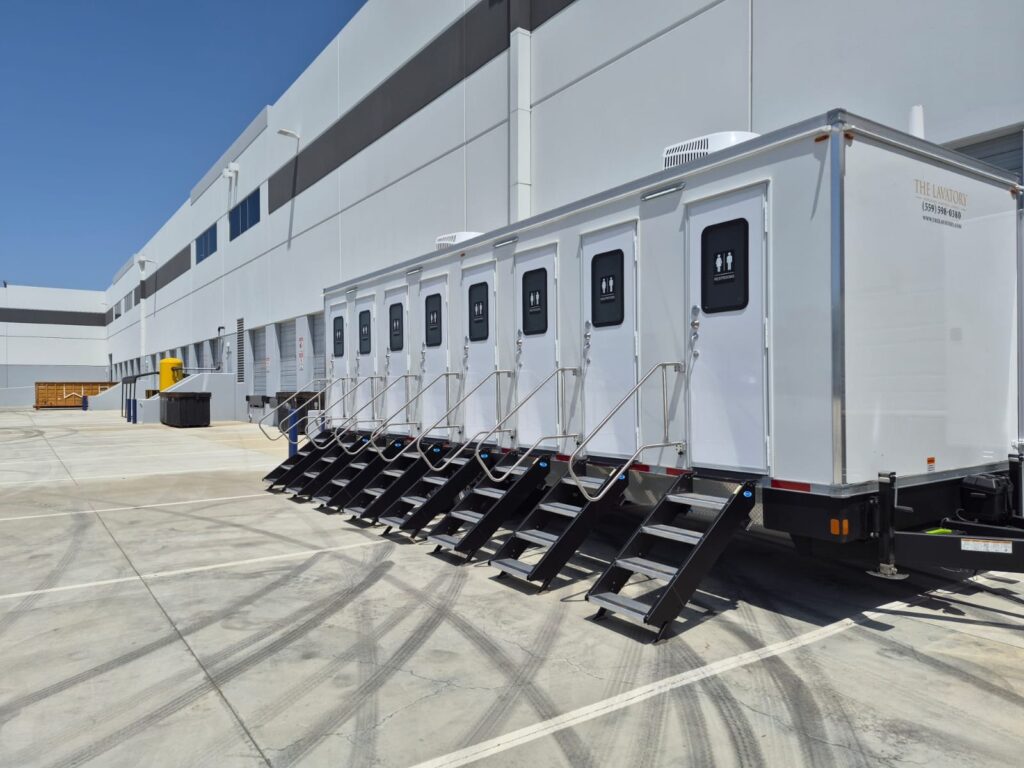 8-station private bathroom trailer with eight doors and stairs parked beside a large warehouse, The Lavatory Los Angeles