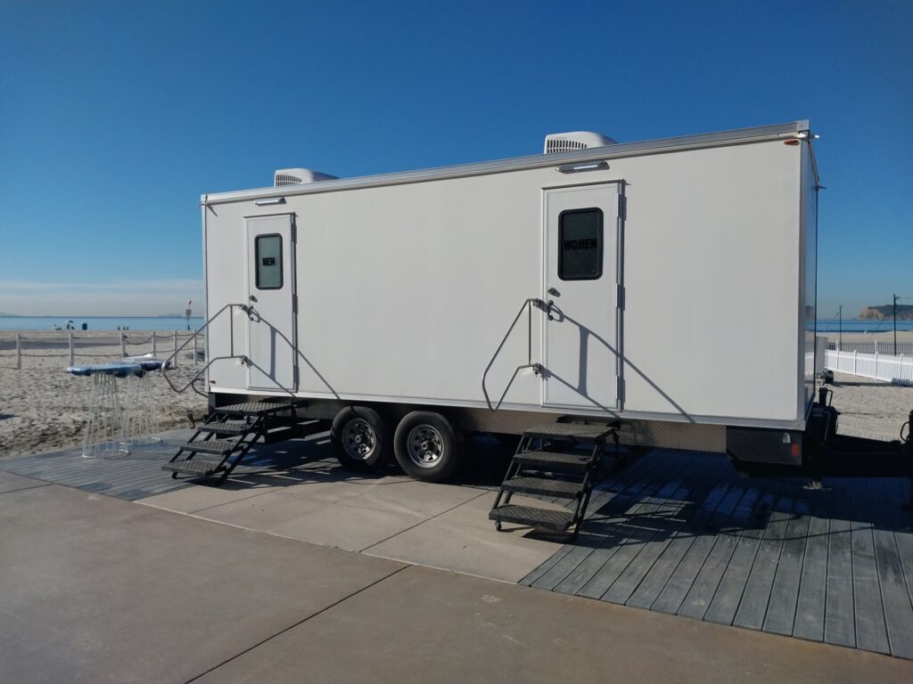 9-station luxury bathroom trailer with men's and women's doors on a deck beside the sand at a beach event, The Lavatory Los Angeles