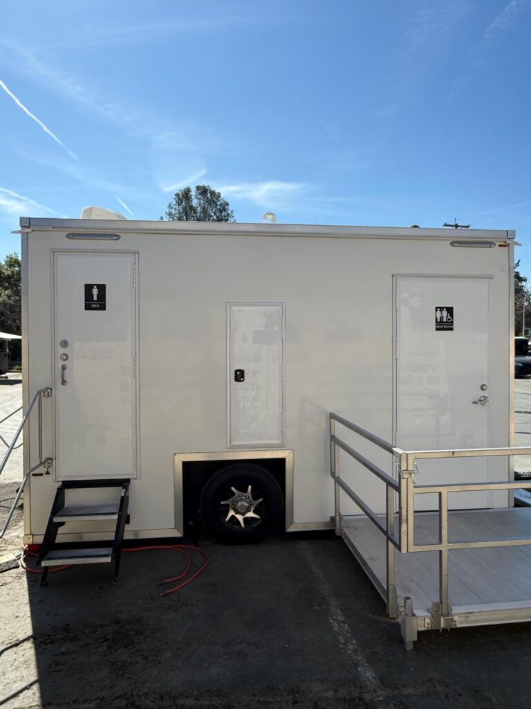 Accessible bathroom trailer with a men's door, a wheelchair access door and a ramp platform hooked up to water on a job site, The Lavatory Los Angeles