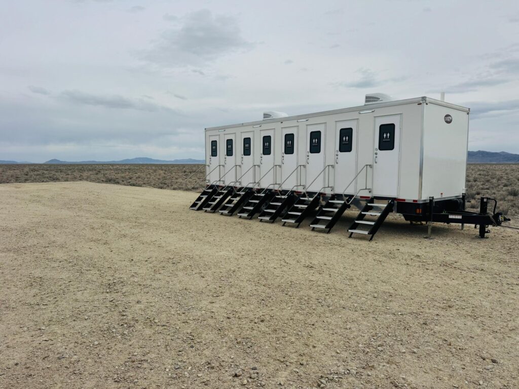 8-station private bathroom trailer with eight private doors and eight sets of stairs on a gravel pad in open high desert scrub, The Lavatory Los Angeles