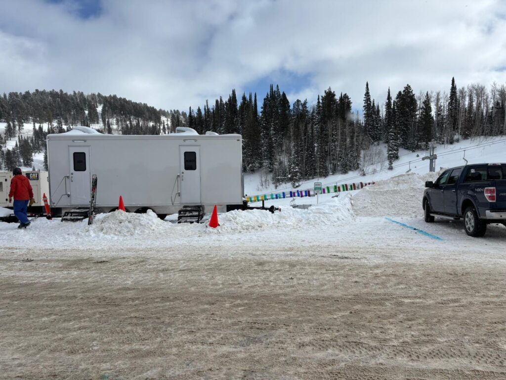 Event staff walking past a long bathroom trailer set on a plowed lot after a snowfall, The Lavatory Los Angeles