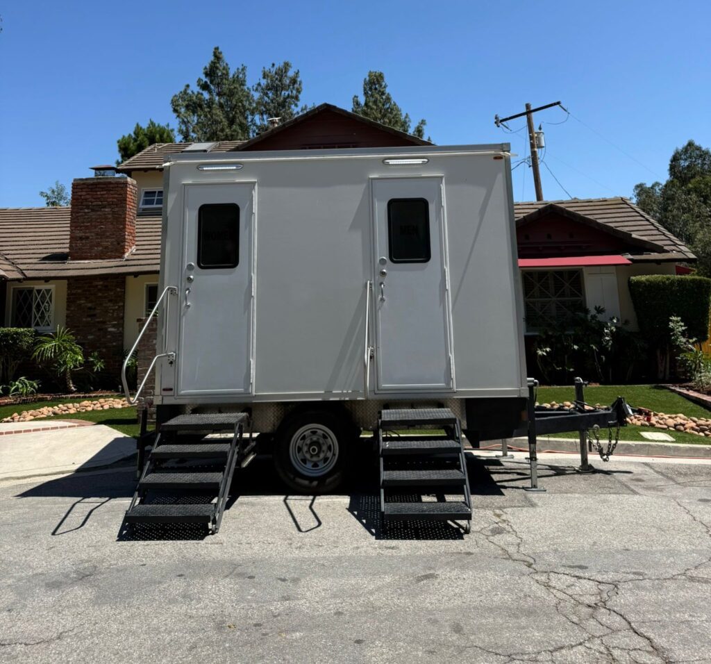 2-station bathroom trailer with two doors and steps parked on a quiet street in front of a brick chimney foothill home, The Lavatory Los Angeles