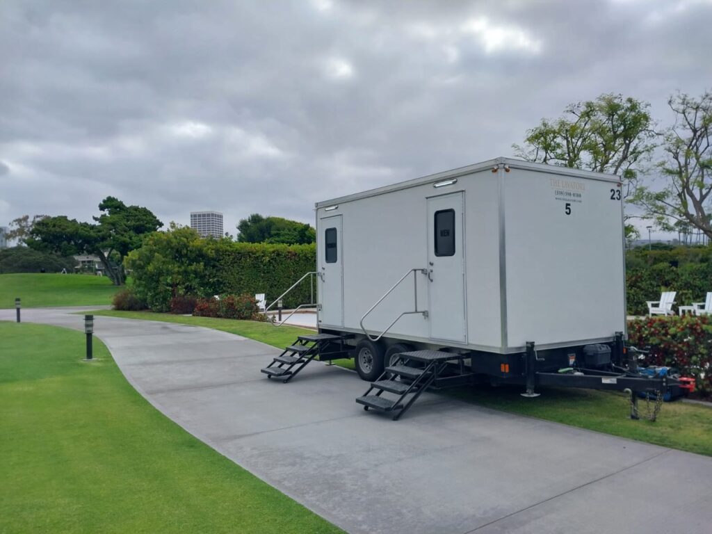 5-station bathroom trailer with men's and women's steps on a golf course cart path beside a green fairway, The Lavatory Los Angeles