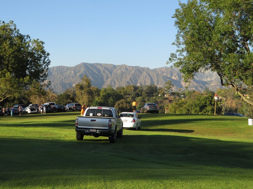 Parking staff in orange vests guiding cars onto the Brookside golf course lawn for a Rose Bowl game, with the San Gabriel Mountains behind, Pasadena, CA, The Lavatory Los Angeles