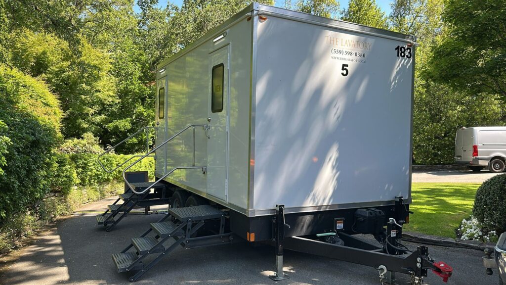 5-station bathroom trailer on a shaded driveway beside a lawn and tall green hedges, The Lavatory Los Angeles