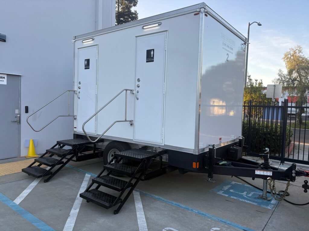 2-station bathroom trailer with railed steps parked beside an office building entrance, The Lavatory Los Angeles