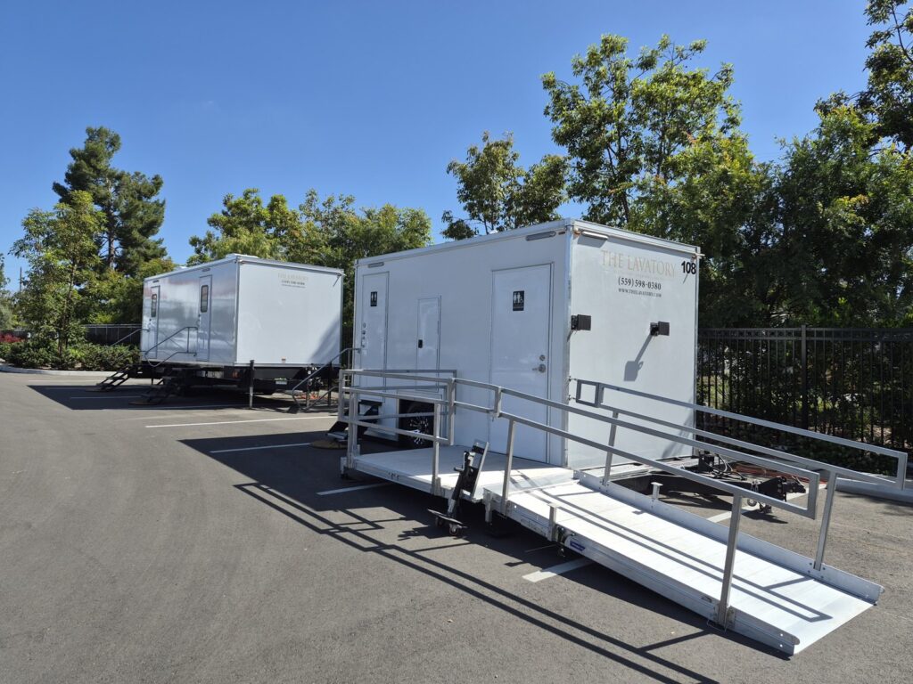 ADA plus 2 bathroom trailer with an aluminum wheelchair ramp and a second bathroom trailer in a parking lot, The Lavatory Los Angeles