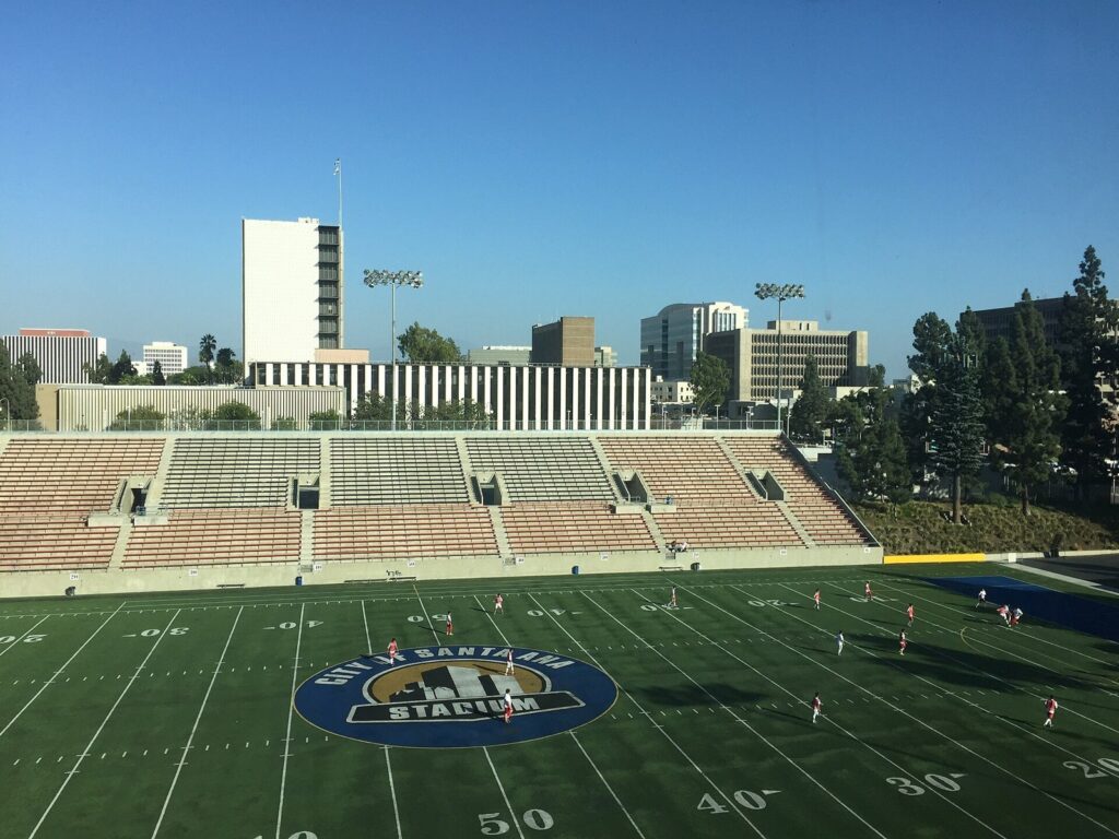 People playing soccer on the field at Santa Ana Stadium with the Civic Center towers behind it, The Lavatory Los Angeles