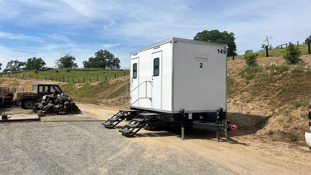 2-station bathroom trailer on a gravel ranch road with cattle grazing on the hillside behind it, The Lavatory Los Angeles