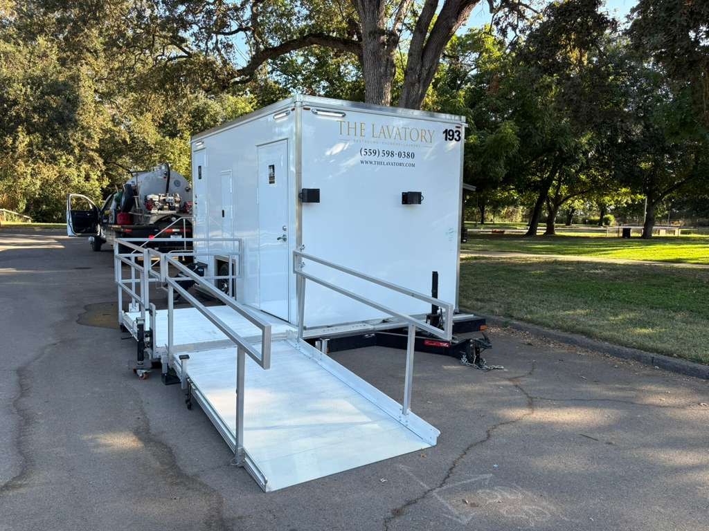 ADA bathroom trailer with an aluminum ramp parked at a park under big oak trees, The Lavatory Los Angeles