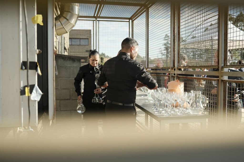 Catering staff in black setting out water glasses and pitchers before an outdoor party, The Lavatory Los Angeles