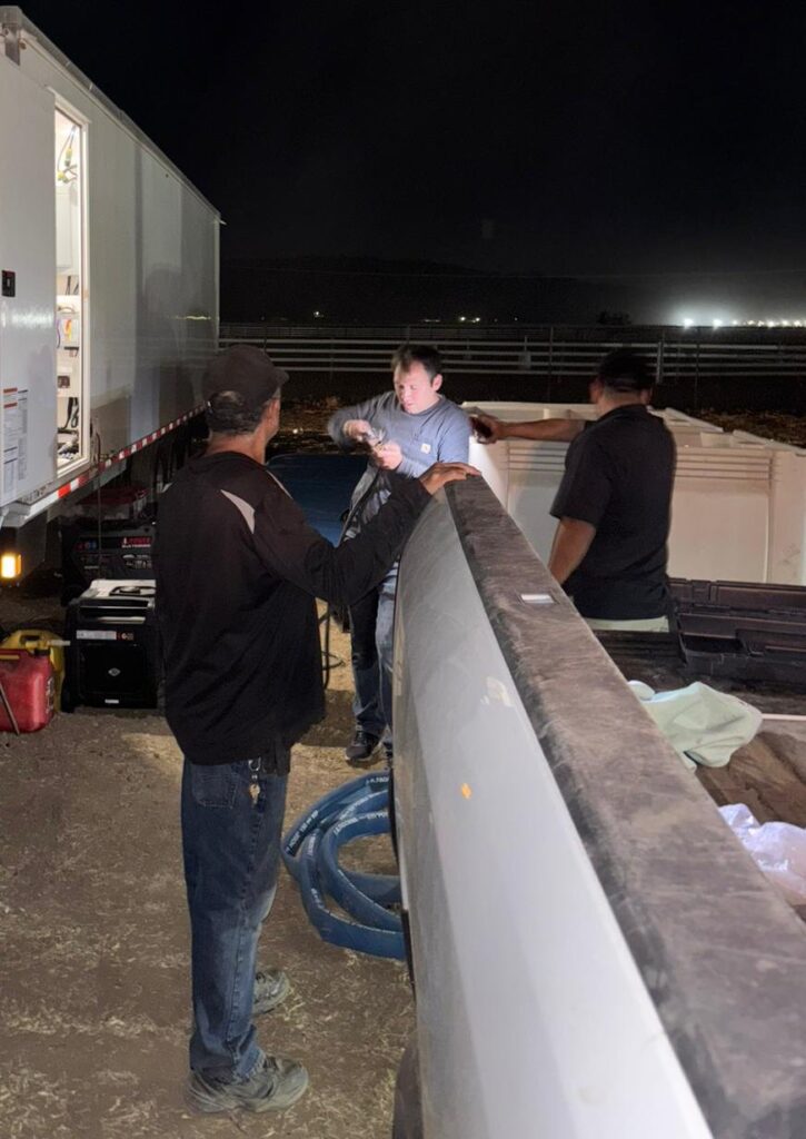 Service team workers checking water and power beside a shower trailer at a remote job site at night, The Lavatory Los Angeles