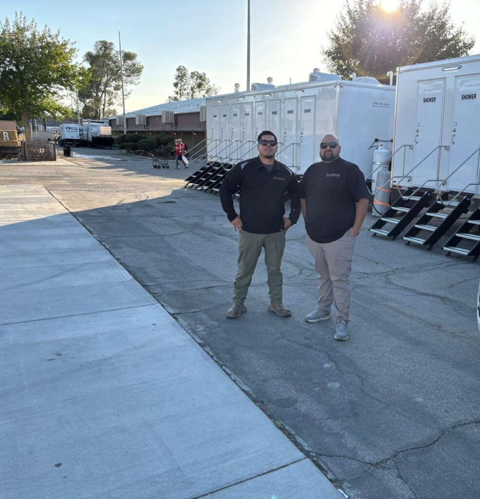 Two members of our team standing beside rows of private shower trailers set up at a fairgrounds lot, The Lavatory Los Angeles