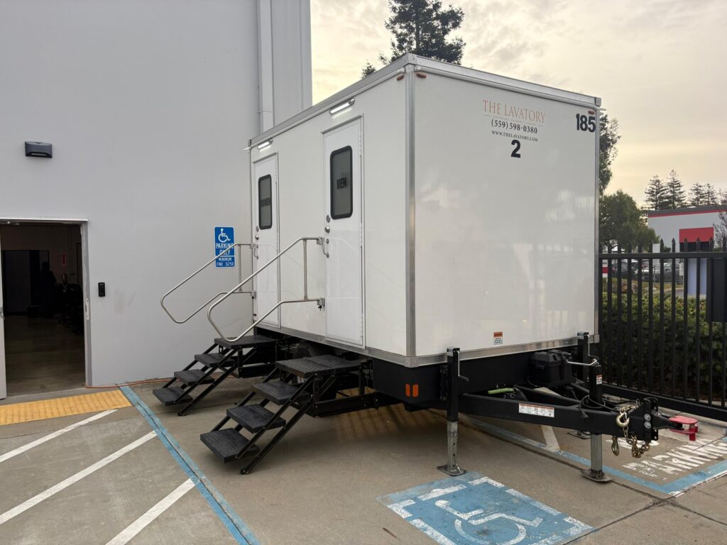 2-station bathroom trailer set beside a building's side door and accessible parking space, The Lavatory Los Angeles