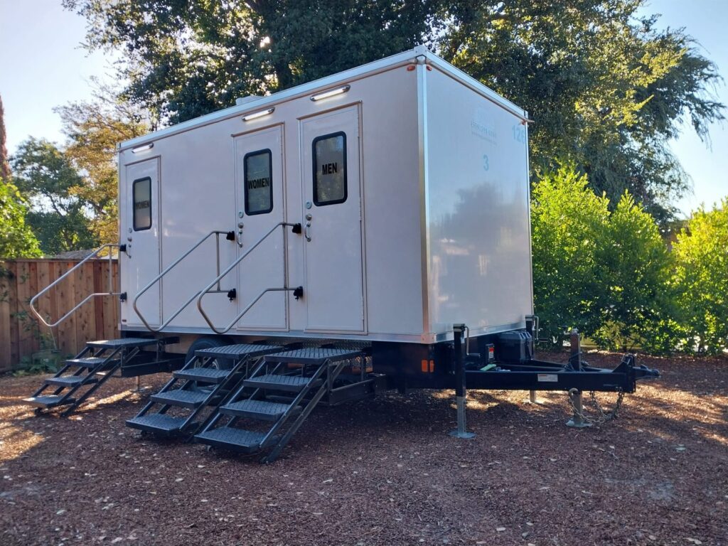 3-station bathroom trailer with three sets of steps on a mulched yard under shade trees, The Lavatory Los Angeles