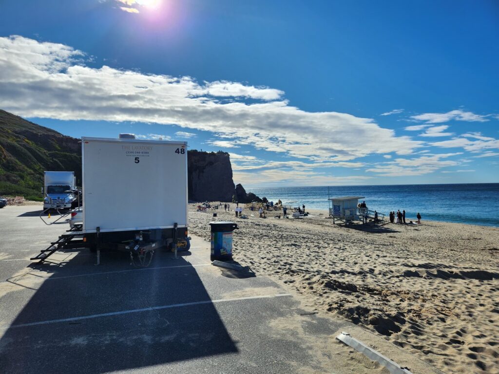 5-station bathroom trailer in a beach parking lot near a production team working on the sand, The Lavatory Los Angeles