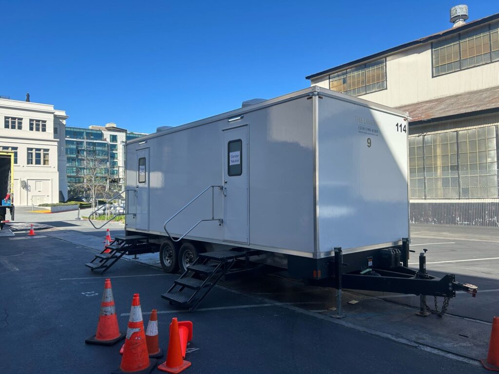 9-station bathroom trailer beside an industrial building with safety cones at the hitch, The Lavatory Los Angeles