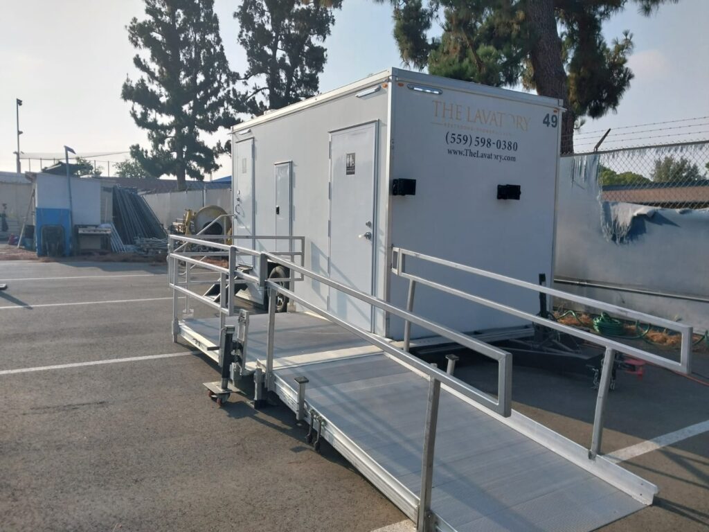 Accessible bathroom trailer with a railed ramp in a fenced work yard, The Lavatory Los Angeles