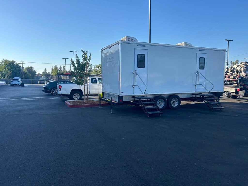 Long tandem-axle bathroom trailer parked across a large retail parking lot, The Lavatory Los Angeles