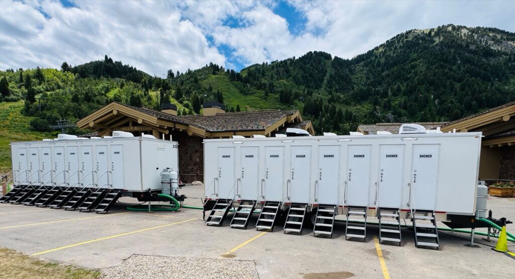 Two 8-station shower trailers lined up in a mountain lodge parking lot with green hillsides behind them, The Lavatory Los Angeles