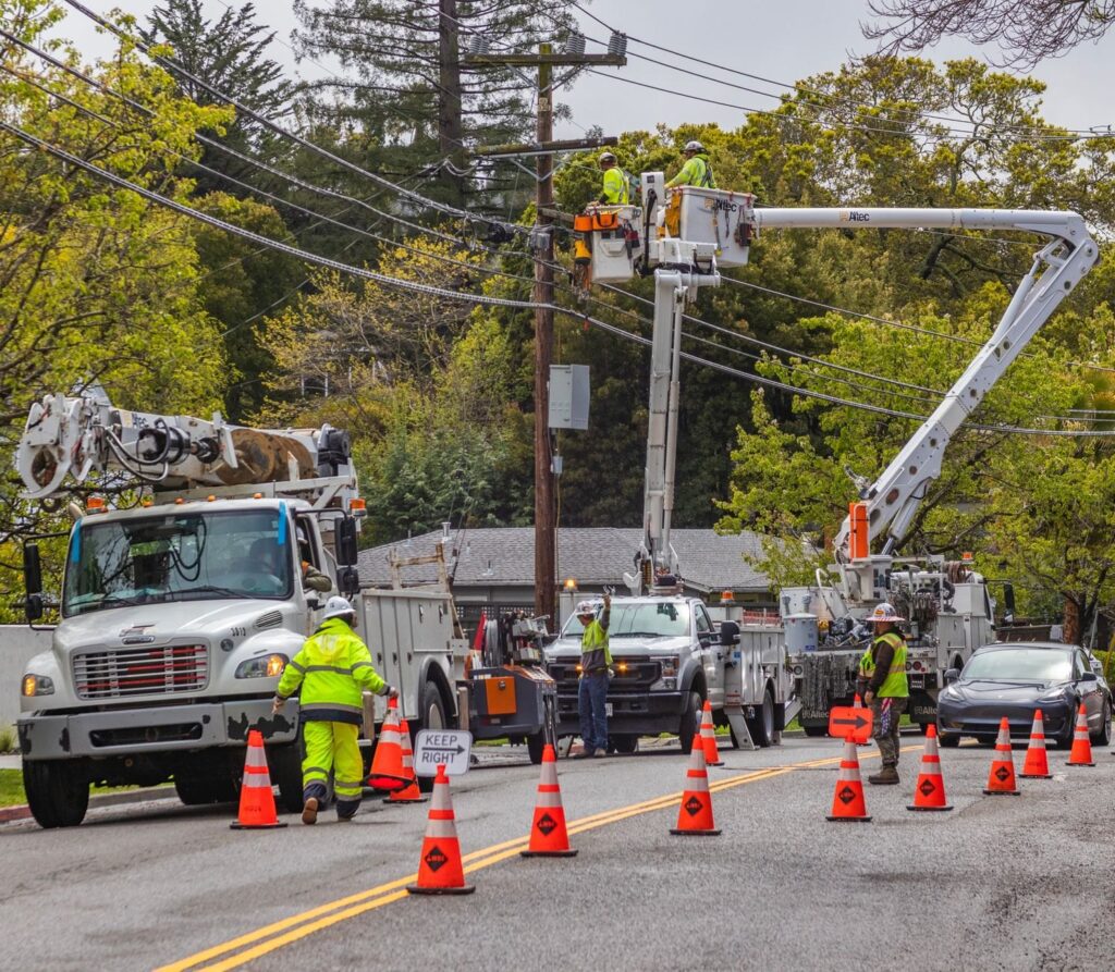 Utility line workers in safety vests repairing power lines from bucket trucks on a coned-off street after a storm, The Lavatory Los Angeles