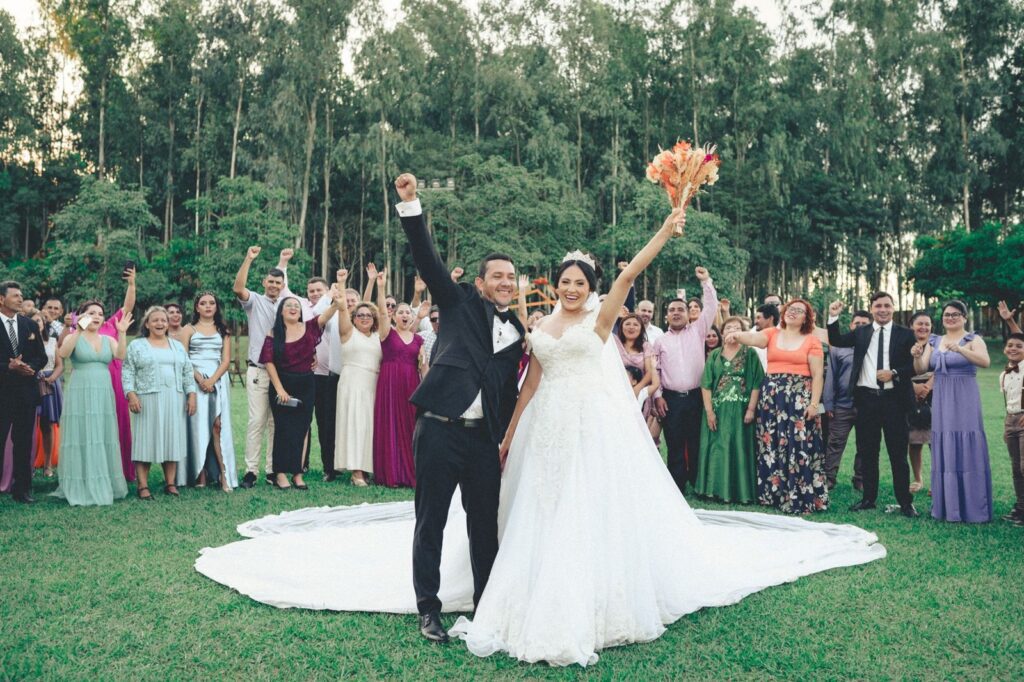 Bride, groom and wedding guests cheering together on a tree-lined lawn after an outdoor ceremony, The Lavatory Los Angeles