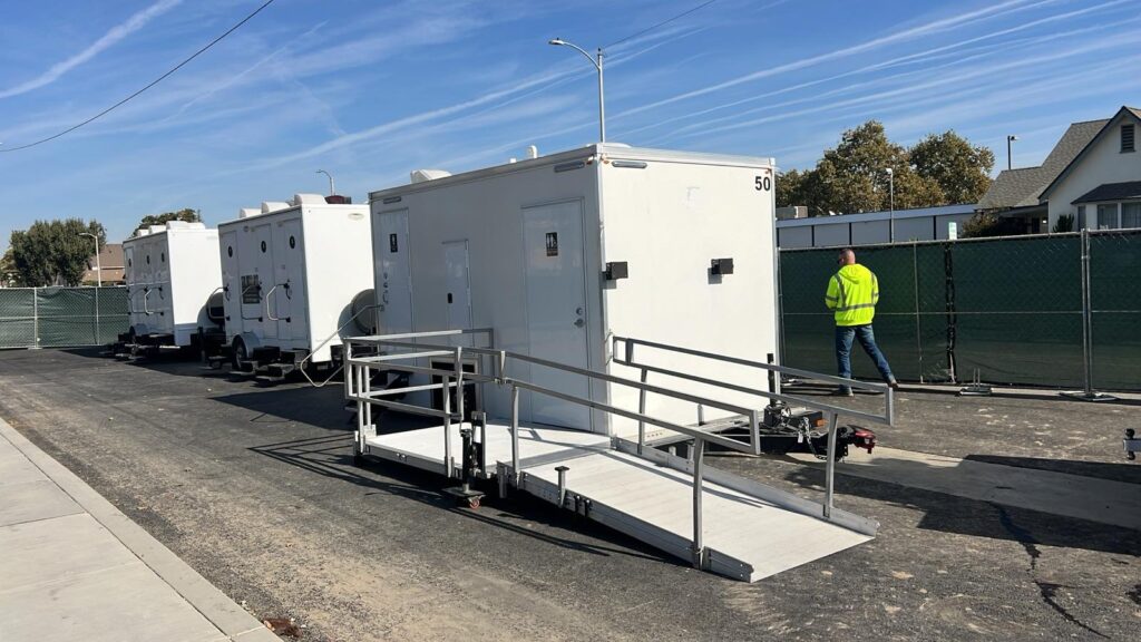 Site worker in a safety vest walking past a row of ADA bathroom trailers with ramps, The Lavatory Los Angeles